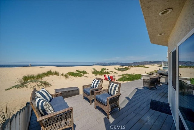 wooden terrace featuring outdoor lounge area, a water view, and a beach view