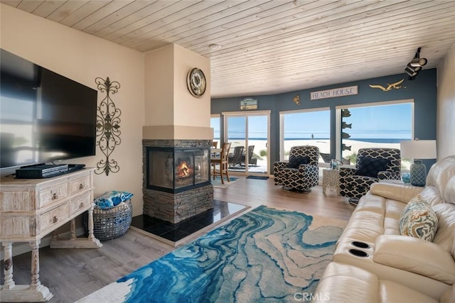 living room with a multi sided fireplace, wood-type flooring, a water view, and wooden ceiling