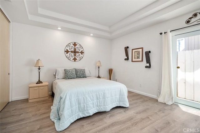 bedroom with light hardwood / wood-style floors and a raised ceiling