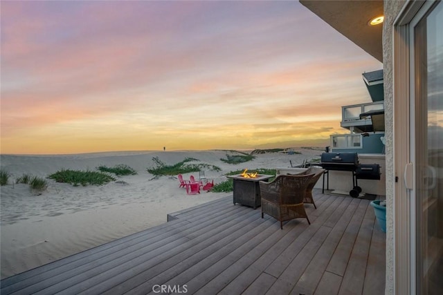 deck at dusk with area for grilling, a water view, and a fire pit