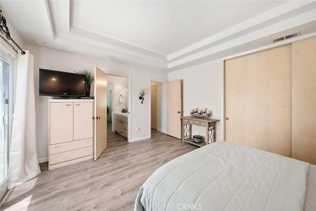 bedroom featuring a raised ceiling, connected bathroom, and light wood-type flooring