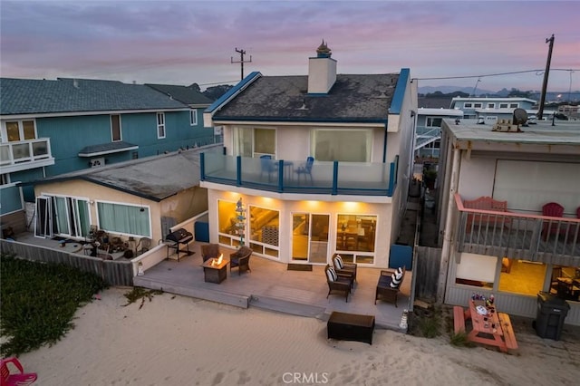 back house at dusk featuring a fire pit and a balcony