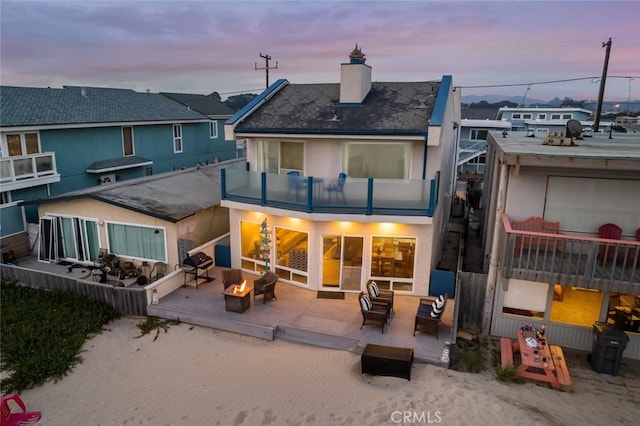 1652 Strand Way, Oceano, CA 93445 - back of house at dusk featuring a balcony, a chimney, stucco siding, and an outdoor living space with a fire pit