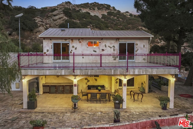 back of property with a mountain view, a patio area, a balcony, and an outdoor living space