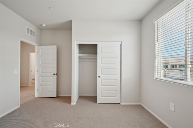 unfurnished bedroom with multiple windows, light carpet, and a closet