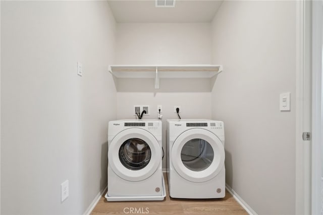 clothes washing area with washer and clothes dryer and light hardwood / wood-style flooring