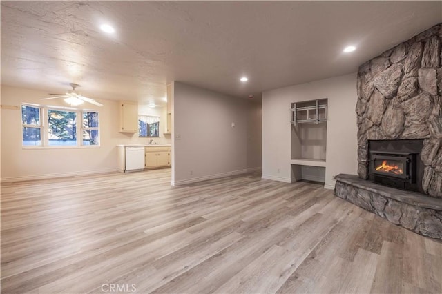 unfurnished living room featuring ceiling fan, sink, a fireplace, and light hardwood / wood-style flooring