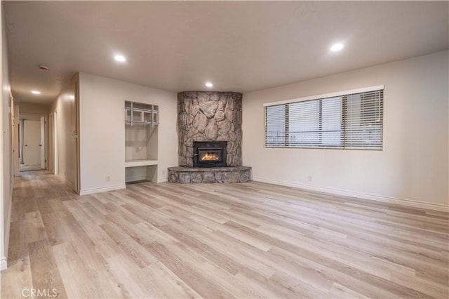 unfurnished living room with a stone fireplace and light wood-type flooring