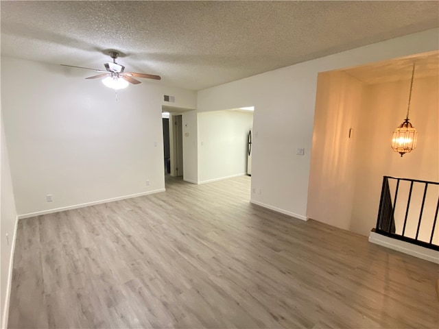 spare room featuring ceiling fan with notable chandelier, visible vents, a textured ceiling, and wood finished floors