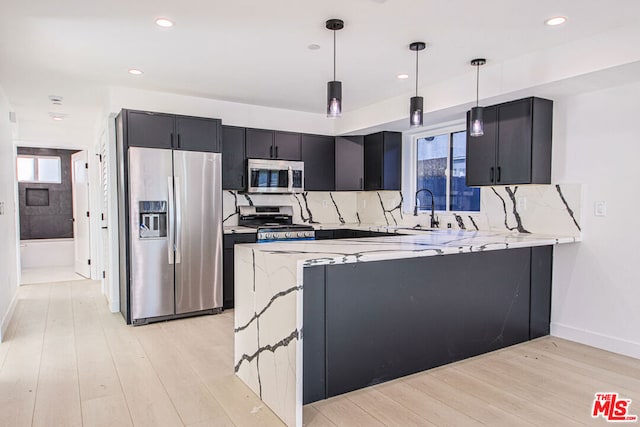 kitchen with pendant lighting, sink, appliances with stainless steel finishes, light stone counters, and kitchen peninsula