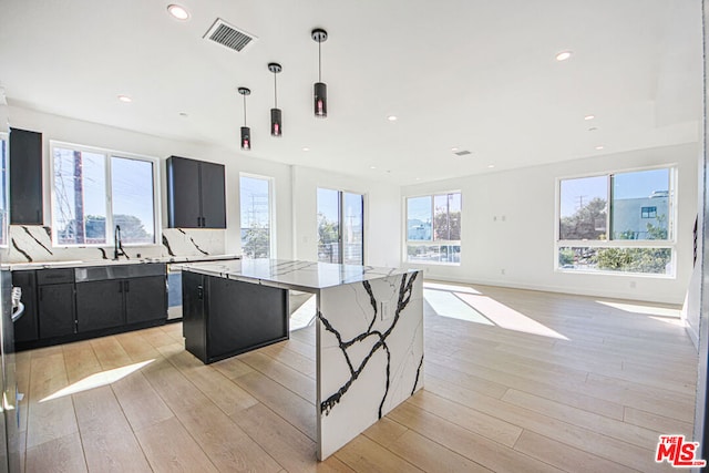 kitchen with a center island, light stone countertops, light wood-type flooring, and hanging light fixtures