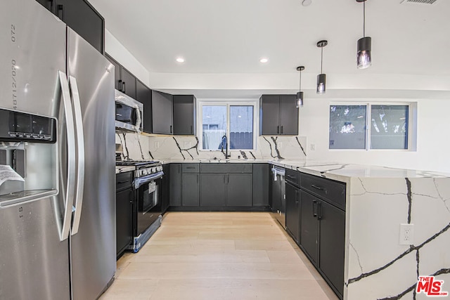 kitchen with pendant lighting, sink, light stone countertops, tasteful backsplash, and stainless steel appliances