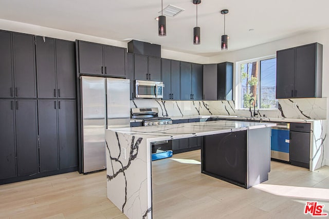 kitchen with appliances with stainless steel finishes, light wood-type flooring, light stone counters, a center island, and hanging light fixtures