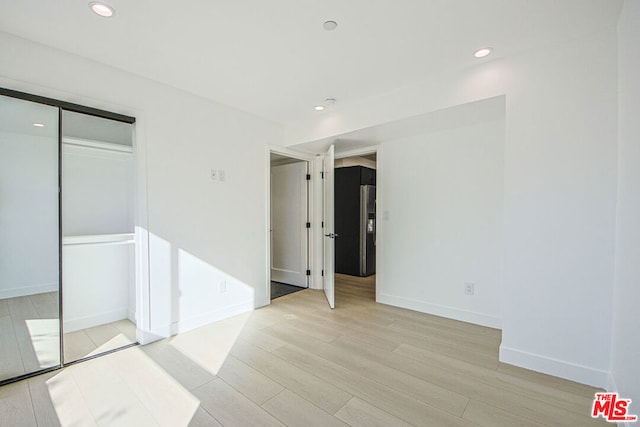 unfurnished bedroom featuring a closet, stainless steel fridge with ice dispenser, and light hardwood / wood-style flooring