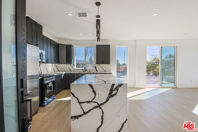 kitchen with pendant lighting, a wealth of natural light, appliances with stainless steel finishes, and light stone counters