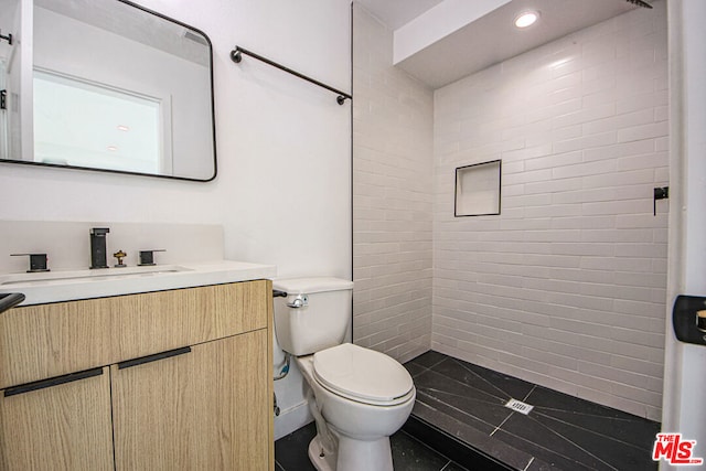 bathroom featuring vanity, toilet, and a tile shower