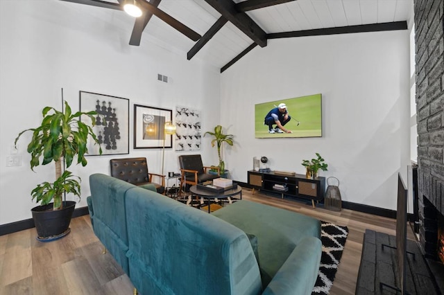 living room with a brick fireplace, ceiling fan, wood-type flooring, high vaulted ceiling, and beamed ceiling