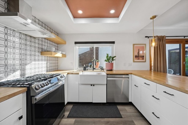 kitchen featuring hanging light fixtures, decorative backsplash, appliances with stainless steel finishes, butcher block countertops, and white cabinetry