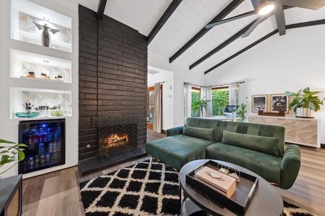 living room featuring beam ceiling, beverage cooler, high vaulted ceiling, wood-type flooring, and a fireplace