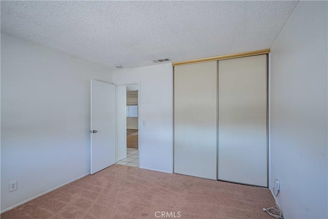 unfurnished bedroom with light carpet, a closet, and a textured ceiling