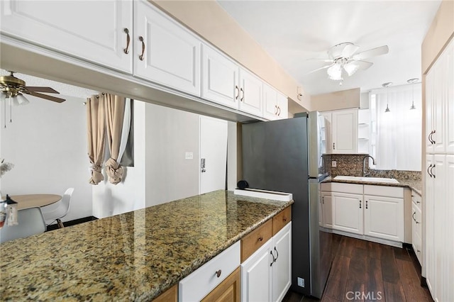 kitchen with tasteful backsplash, dark wood-type flooring, sink, dark stone countertops, and white cabinets