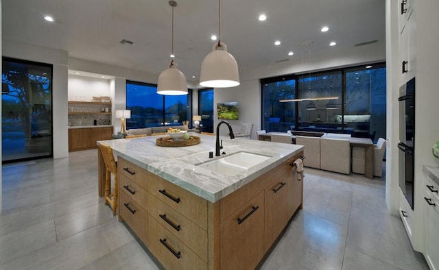 kitchen featuring white cabinets, sink, hanging light fixtures, a large island, and light stone counters