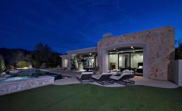 back house at twilight with a swimming pool with hot tub, an outdoor living space, and a patio area