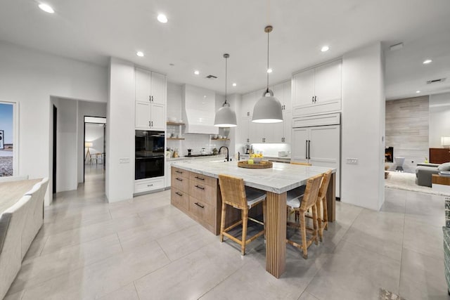 kitchen featuring a large island with sink, decorative light fixtures, white cabinetry, and light stone counters