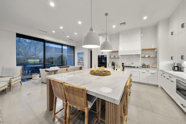 kitchen featuring white cabinets, pendant lighting, light stone counters, and a spacious island