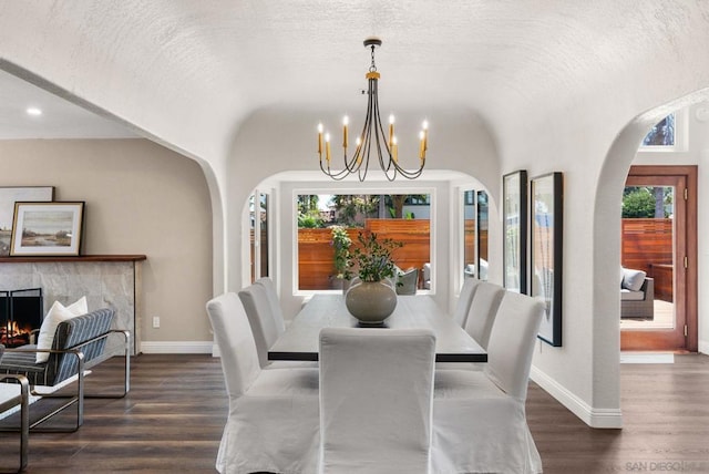 dining room featuring lofted ceiling, a high end fireplace, dark hardwood / wood-style flooring, and a notable chandelier