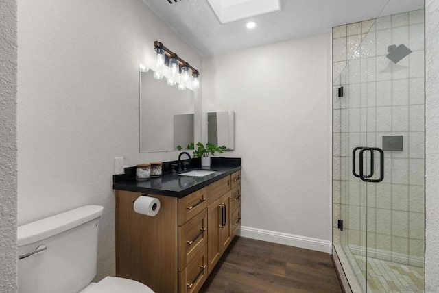 bathroom featuring toilet, a skylight, hardwood / wood-style flooring, a shower with door, and vanity