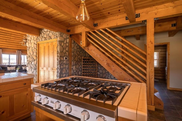 kitchen featuring wood ceiling, dark tile patterned floors, tile countertops, beamed ceiling, and stainless steel gas stovetop