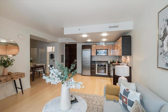 living room with stacked washer / dryer, sink, and light hardwood / wood-style flooring