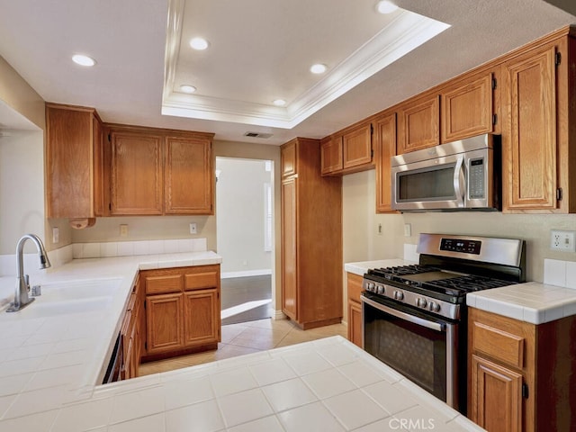 kitchen featuring tile countertops, stainless steel appliances, a raised ceiling, ornamental molding, and sink