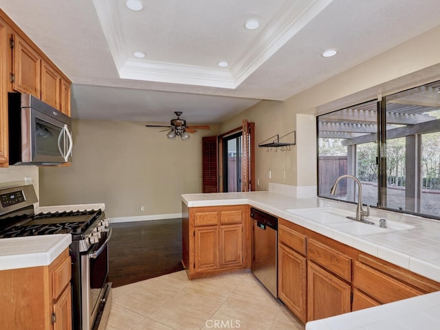 kitchen featuring tile countertops, a raised ceiling, kitchen peninsula, sink, and appliances with stainless steel finishes