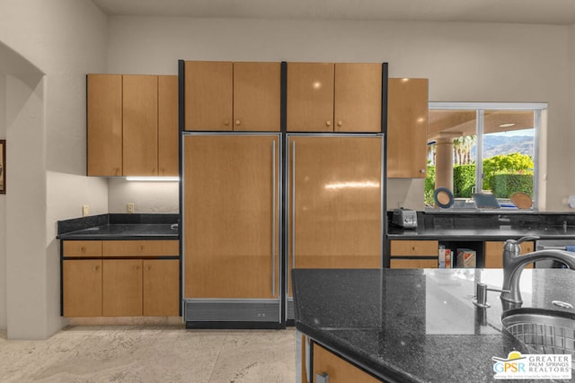 kitchen with paneled fridge, dark stone counters, and sink