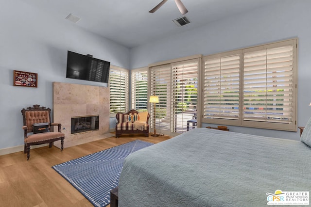 bedroom with a fireplace, hardwood / wood-style flooring, multiple windows, and ceiling fan