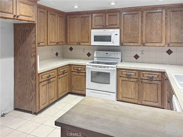 kitchen featuring tile counters, light tile patterned floors, decorative backsplash, and white appliances