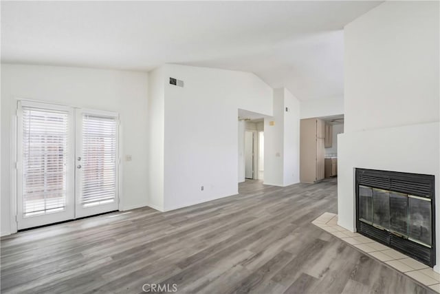 unfurnished living room featuring a tiled fireplace, lofted ceiling, french doors, and light hardwood / wood-style flooring