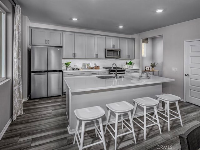 kitchen featuring gray cabinetry, sink, stainless steel appliances, dark wood-type flooring, and a kitchen island with sink