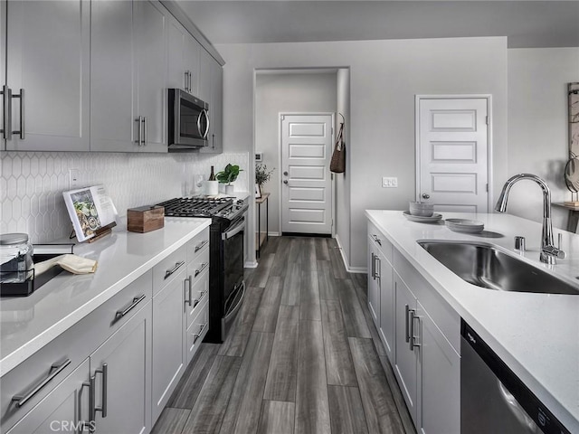 kitchen with decorative backsplash, gray cabinetry, stainless steel appliances, dark wood-type flooring, and sink