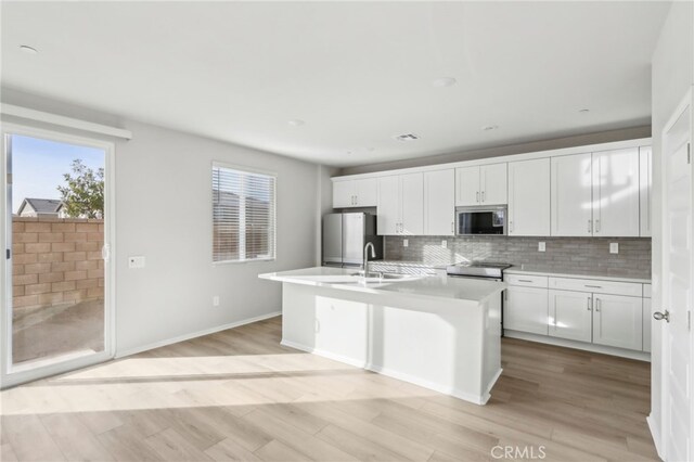 kitchen featuring backsplash, stainless steel appliances, an island with sink, and white cabinets