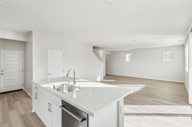 kitchen with an island with sink, dishwasher, sink, white cabinets, and light wood-type flooring