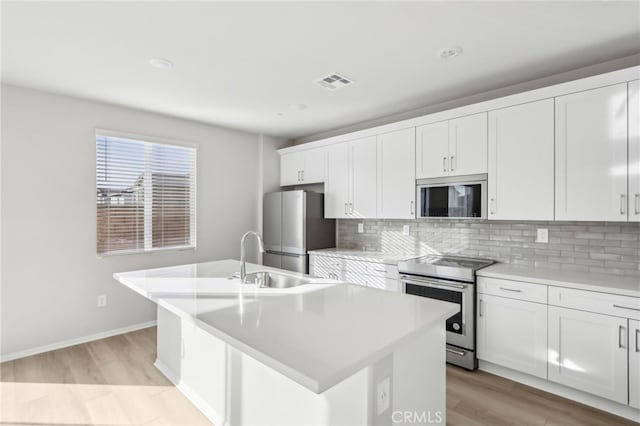 kitchen with tasteful backsplash, white cabinetry, light hardwood / wood-style floors, stainless steel appliances, and a center island with sink