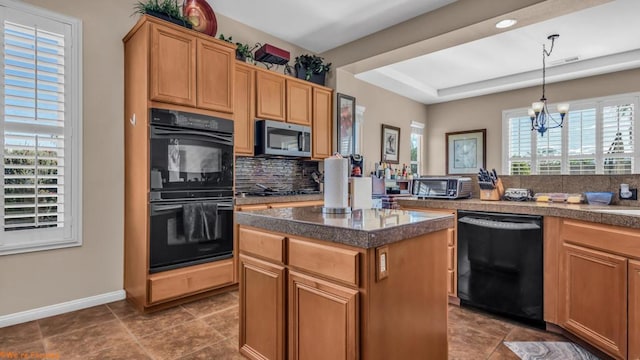 kitchen featuring a center island, black appliances, a tray ceiling, hanging light fixtures, and a chandelier