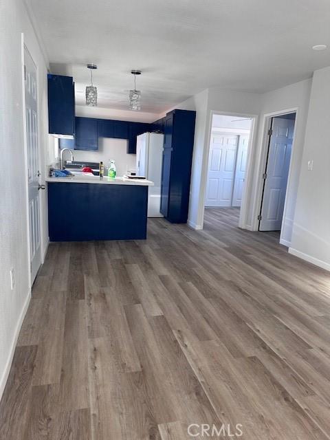 kitchen with hardwood / wood-style flooring, white fridge, kitchen peninsula, and blue cabinets