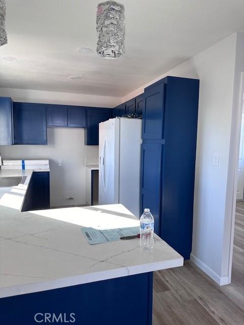 kitchen featuring white refrigerator with ice dispenser, hardwood / wood-style flooring, and blue cabinets