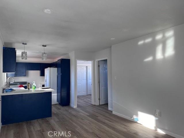 kitchen featuring blue cabinetry, sink, dark wood-type flooring, white refrigerator, and kitchen peninsula