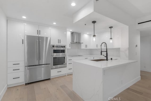 kitchen featuring sink, wall chimney exhaust hood, decorative light fixtures, kitchen peninsula, and stainless steel appliances