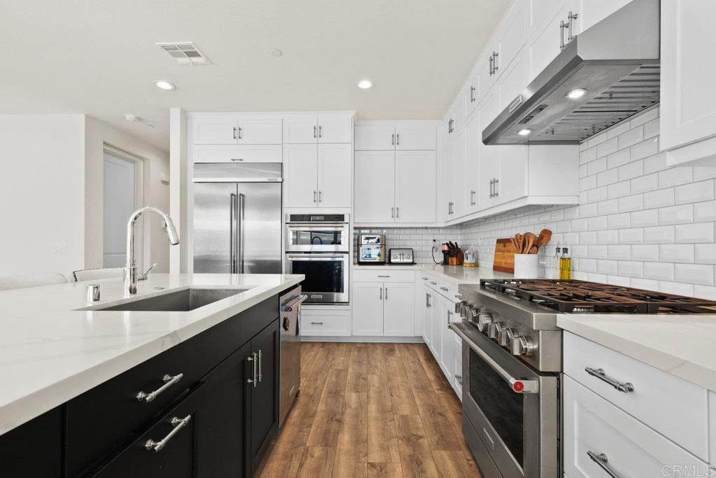 kitchen with sink, light stone counters, premium appliances, white cabinets, and decorative backsplash